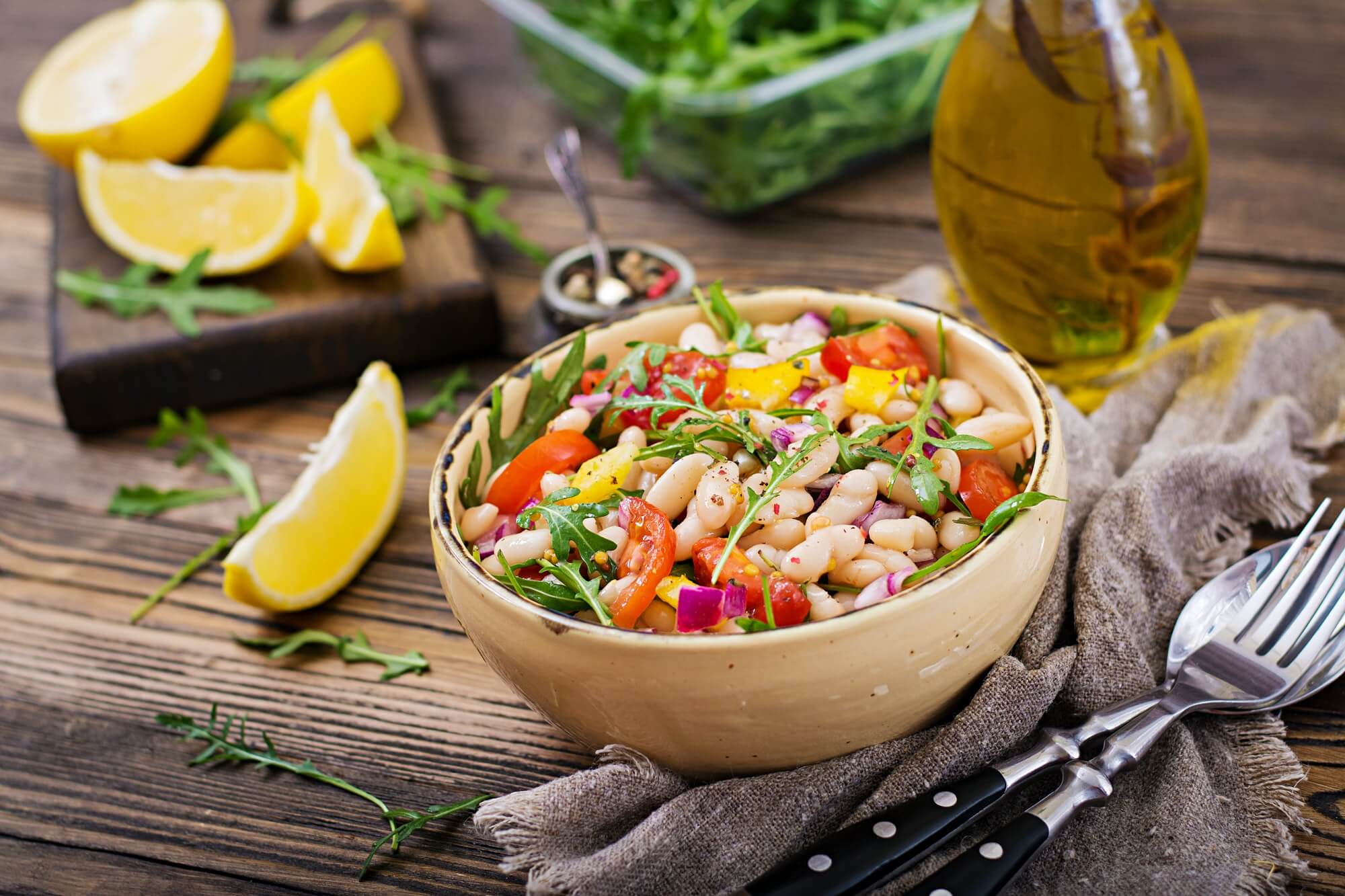 A bowl of salad on a wooden table with lemons and dressing